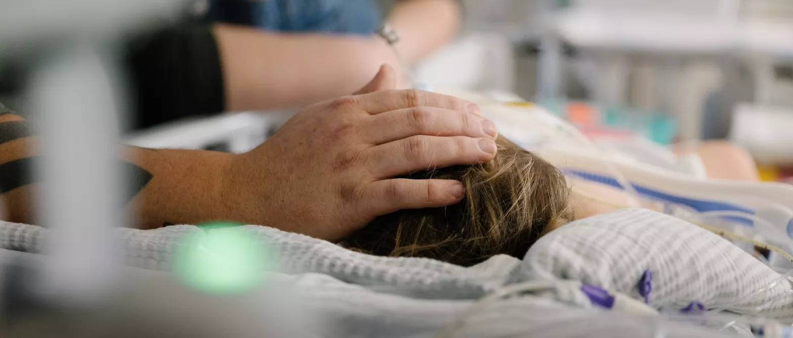 A caring hand on a patient's head as they lie in a hospital bed