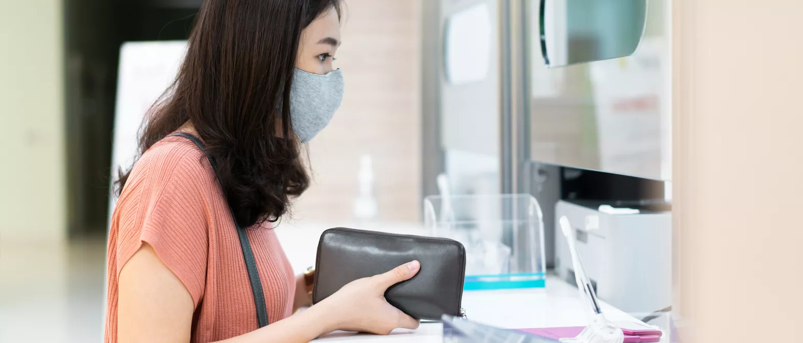 Woman in mask holding wallet by cashier window