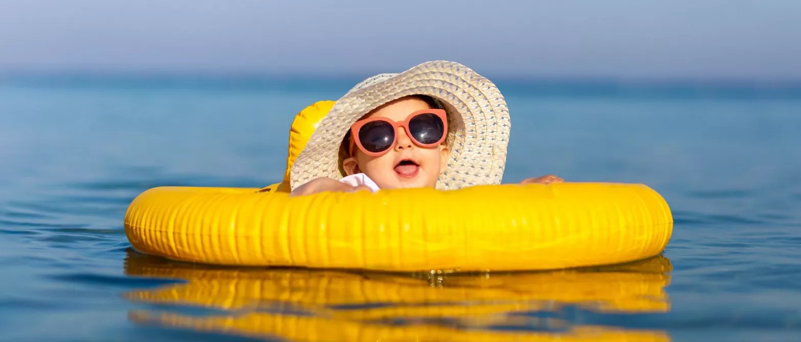 Baby in sunhat and sunglasses swimming with floatie