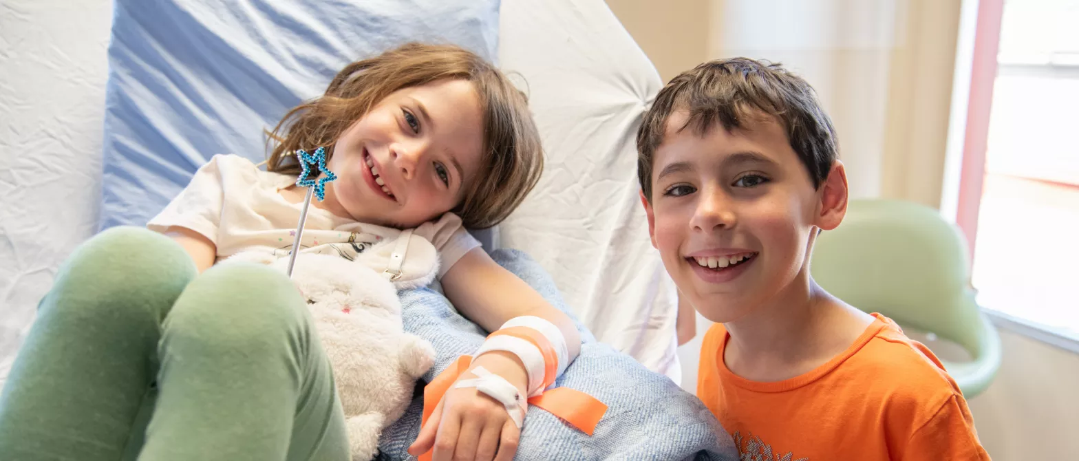 A child smiling while visiting their sibling in a hospital bed. 