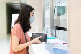 Woman in mask holding wallet by cashier window