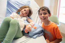 A child smiling while visiting their sibling in a hospital bed. 
